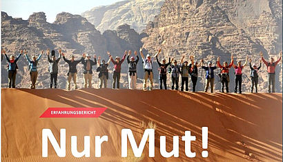 Ein Ausschnitt des Liudger-Titelbildes mit der Aufschrift "Nur Mut!" zeigt achtzehn Frauen und Männer mit jubelnd erhobenen Armen nebeneinander auf einer Düne in der jordanischen Wüste. Im Hintergrund Gebirge und blauer Himmel.